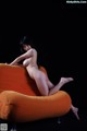 A naked woman sitting on an orange chair.